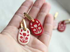 two small red and white flowered pendants in someone's hand