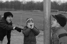 three young boys standing next to each other near a baseball field with one boy holding his mouth open