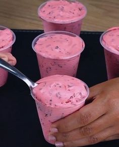 pink ice cream in plastic cups being held by someone's hand with a spoon