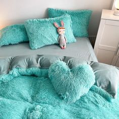 a bed covered in blue fluffy pillows with a bunny stuffed animal on it's head