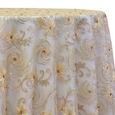 a white table cloth with gold flowers and swirls on the top, along with a lace edge