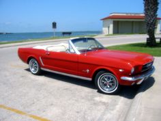 an old red mustang convertible parked on the side of the road next to the ocean