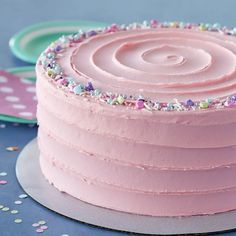 a pink frosted cake with sprinkles sits on a plate next to confetti