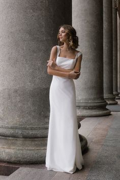 a woman in a white dress standing next to some pillars and looking off into the distance