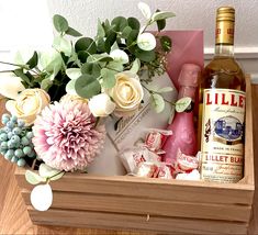 a wooden box filled with bottles and flowers next to a bottle of wine on top of a table