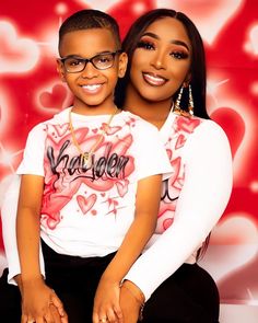 two people sitting next to each other in front of a red wall with hearts on it