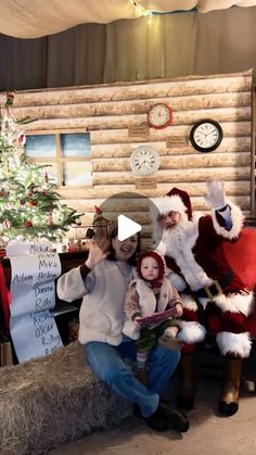 two people dressed as santa claus and holding a child in front of a christmas tree