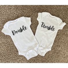 two white onesuits with the words double and trouble printed on them sitting on carpet