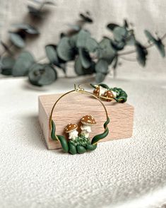 a pair of hoop earrings with mushrooms and leaves on them sitting on a wooden block