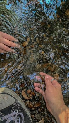 two hands reaching for something in the water with rocks and pebbles on the ground next to them