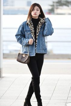 a woman wearing black boots and a denim jacket with leopard print on the collar, holding a handbag