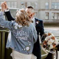 a bride and groom standing next to an old car with their arms in the air