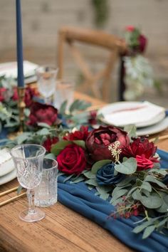 the table is set with red and blue flowers, greenery and candlesticks