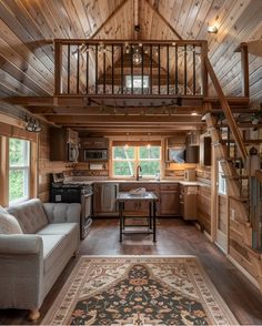 a living room and kitchen inside of a wooden cabin with stairs leading up to the loft