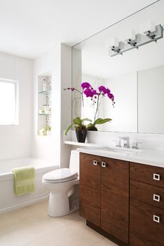 a white toilet sitting next to a bath tub in a bathroom under a mirror with purple flowers on it