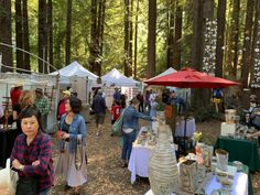 a group of people standing around tables with food on them in the middle of a forest