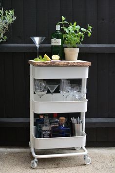 a bar cart with wine glasses, bottles and lemons on the top is sitting next to a potted plant