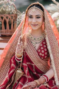 a woman in a red and gold bridal outfit sitting on a bench with her hands behind her head