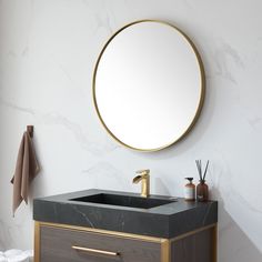 a bathroom vanity with marble counter top and gold faucet, round mirror above it