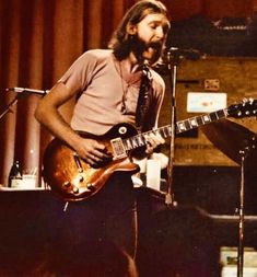 a man with long hair playing an electric guitar in front of microphones on stage