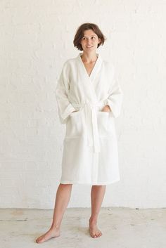 a woman standing in front of a white wall wearing a robe and pink slippers