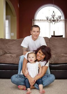 a man and woman sitting on the floor with a baby in their lap, smiling at the camera