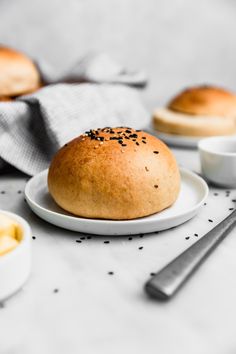 a bun sitting on top of a white plate next to two bowls of mustard and spoons