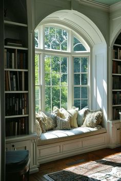 a window seat with pillows on it in front of a bookshelf