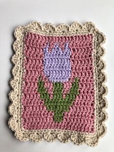 a crocheted square with a purple flower on it and scalloped edges