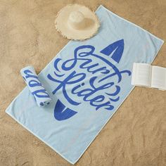 a towel, book and hat laying on the sand