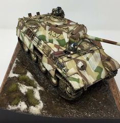 a camouflaged tank is sitting on top of a wooden base with snow around it