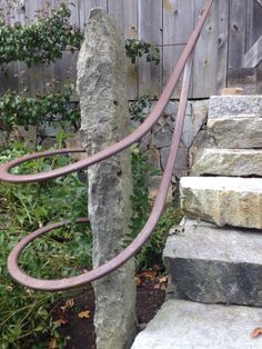 a metal hose is attached to a stone wall next to some rocks and plants in front of a wooden fence