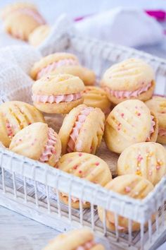 a basket filled with pink frosted cookies on top of a wooden table next to a white cloth