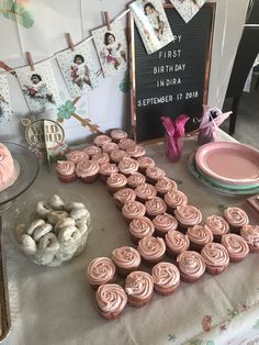 a table topped with lots of cupcakes covered in frosting next to a sign