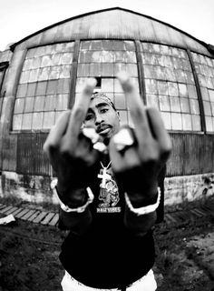 a black and white photo of a man making the v sign with his hands in front of a building