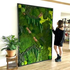 a woman standing in front of a moss covered wall with plants and rocks on it