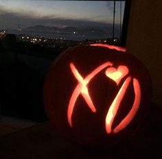 a pumpkin carved to look like an x on top of a window sill with the city lights in the background