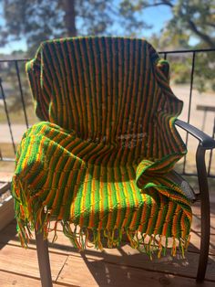 a green and yellow blanket sitting on top of a wooden deck next to a chair