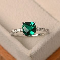 an emerald colored ring with diamond accents in a box