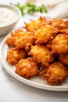 some fried food on a white plate next to a bowl of ranch dressing and dip