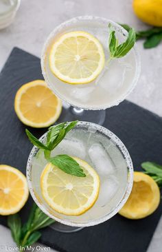 two margaritas with lemon slices and mint garnish sit on a black mat