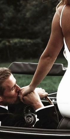 a woman in a white dress kissing a man in a black and white convertible car