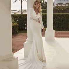 a woman in a white wedding dress standing on a porch with columns and palm trees