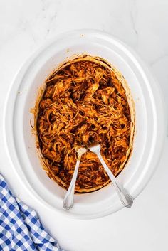 a white bowl filled with shredded meat on top of a table next to a blue and white checkered napkin