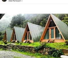 a group of wooden cabins sitting on top of a lush green hillside next to a forest