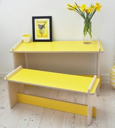 a yellow bench sitting in front of a vase with flowers on it and a framed picture