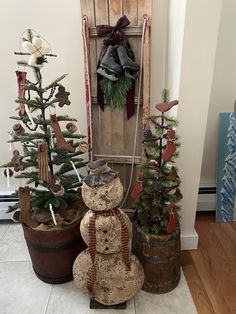 a snowman and two christmas trees in front of a wooden door with decorations on it