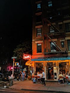 people are walking on the sidewalk in front of a building with neon signs and stairs