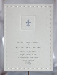 a white wedding card with a blue fleur de lis stamp on the front