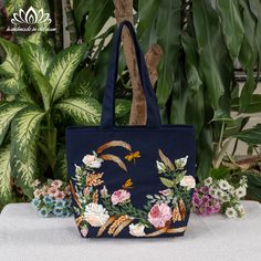 a blue bag with flowers and birds on it sitting on a table in front of some plants